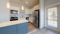 Located at 3 Gilbert Dr in Merrimack, New Hampshire, this single-floor residence offers a thoughtfully designed layout with modern finishes throughout. The open-concept living and kitchen area serves as the heart of the home, featuring durable hardwood-style plank flooring that flows seamlessly across the space. Large windows invite an abundance of natural light into the living area, offering views of the surrounding neighborhood.

The kitchen is well-appointed with crisp white cabinetry extending to the ceiling for generous storage, light-toned countertops, and a full suite of stainless steel appliances including a refrigerator, range, microwave, and dishwasher. A central island with a contrasting slate-blue finish provides additional prep space and casual seating, while pendant lighting adds a stylish focal point overhead. Recessed lighting throughout ensures the space remains bright and functional.

The bedroom is finished with plush carpeting for comfort and features a set of double doors leading to a spacious closet, providing ample storage. Soft, neutral wall tones carry throughout the entire residence, contributing to a calm and cohesive aesthetic. The bathroom is finished with wood-look tile flooring, a vanity with cabinetry, and clean white fixtures, offering a tidy and functional space. Overall, this residence presents a clean, contemporary living environment with practical amenities and a welcoming ambiance.