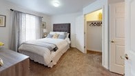 This single-floor residence offers a well-organized layout with distinct living spaces designed for everyday comfort and practicality. The kitchen is outfitted with warm honey-toned oak cabinetry providing generous upper and lower storage, white appliances including a refrigerator, electric range, and dishwasher, complemented by light countertops and a double sink. Hardwood-style flooring runs through the kitchen and dining area, where space accommodates a small dining table. An archway transitions into the living room, which features plush carpeting, a large sliding glass door that brings in natural light and outdoor views, and a ceiling fan overhead. A secondary flexible room, also carpeted, includes a window with outdoor views and functions well as a home office or additional lounge space. The bedroom is comfortably sized with soft carpet, a window with sheer curtains, and an adjoining closet offering dedicated storage. The bathroom includes a full tub-shower combination with a curtain, hardwood-style flooring, and safety grab bars installed along the walls, adding a practical accessibility feature to the space.