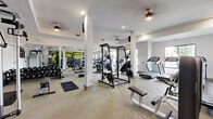 Located at 9015 Eager Rd in Richmond Heights, MO, this fitness center offers a spacious, single-floor layout designed to support a full range of workout routines. The space is thoughtfully organized into distinct zones, accommodating both cardio and strength training needs.

The cardio area is outfitted with treadmills, ellipticals, and a rowing machine, positioned near large windows that invite natural light and provide outdoor views, creating an energizing atmosphere for endurance workouts. Ceiling fans are distributed throughout, ensuring comfortable airflow across the floor.

The strength training section features a power rack with weight plates, a cable machine, adjustable benches, a full dumbbell rack, and kettlebells — offering extensive options for resistance training. Full-length mirrors line sections of the walls, enhancing the sense of openness while allowing users to monitor their form.

A bold motivational mural anchors one end of the space, adding a vibrant visual focal point alongside a dual water fountain station for convenient hydration. Wall-mounted flat-screen televisions and ceiling-mounted speakers contribute to an engaging workout environment.

The neutral-toned flooring, white walls, and recessed lighting give the facility a clean, modern aesthetic. The overall design balances functionality with a welcoming ambiance, making it a well-rounded fitness destination.