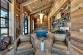 Located in Bozeman, Montana, this single-floor amenity space masterfully blends rustic mountain character with modern functionality. The interior is defined by reclaimed wood planking that covers the walls and ceilings throughout the primary gathering areas, creating a warm, lodge-inspired atmosphere complemented by light hardwood flooring and pendant lighting.

The main recreation room serves as the heart of the space, centered around a full-sized pool table beneath globe pendant lights. A reclaimed wood bar with industrial stools anchors one corner, while industrial pipe shelving along one wall provides organized storage for outdoor gear, including fishing vests, packs, and equipment — perfectly suited to the active Montana lifestyle. Vintage snowshoes and maps add to the rugged aesthetic.

Adjacent to the game room, a comfortable lounge area features leather sofas, a wall-mounted flat-screen TV, and large black-framed windows that invite abundant natural light and street views. The space accommodates bikes and paddle boards, reflecting its outdoor recreation focus.

In striking contrast, the utility area presents a clean, bright wash bay with sealed epoxy flooring, white tile walls, stainless steel utility sinks, a glass-panel garage door, and high vaulted ceilings with overhead lighting — ideal for rinsing gear or equipment. A modern bathroom completes the space, finished with gray subway tile, white tile flooring, and a sleek vanity with backlit mirror.