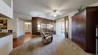 This thoughtfully designed single-floor residence offers a comfortable and functional layout across several well-defined living spaces. The expansive living room serves as the heart of the home, featuring plush carpeting, crown molding, a ceiling fan, and a rich accent wall in warm chocolate brown. A sliding glass door opens directly to a private balcony, inviting natural light and outdoor views into the space. Adjacent to the living area, the dining space features warm hardwood-style flooring and crown molding, creating a seamless transition from the kitchen.

The galley-style kitchen is efficiently laid out with light wood cabinetry, dark countertops, a full suite of white appliances, a double sink, and durable hardwood-style flooring. A hallway leads from the kitchen to a dedicated in-unit laundry room equipped with side-by-side washer and dryer units.

The residence includes two bedrooms, both carpeted and filled with natural light from large windows dressed with decorative valances and vertical blinds. The bathroom is outfitted with rich hardwood-style flooring, a generous vanity with white cabinetry, a well-lit mirror, and ample counter space. Overall, the space presents a warm, cohesive aesthetic with consistent finishes throughout.