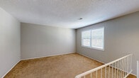 Located at 908 Bellomondo Dr in Platte City, Missouri, this two-bedroom, one-bathroom home offers a practical and well-organized layout across a single floor. A staircase leads up to the main living area, where a pendant light and white railing create a welcoming entry point. The living room is bright and open, featuring plush carpet, neutral gray walls, and a large window that fills the space with natural light. Sliding glass doors lead out to a balcony overlooking a lush, green outdoor setting — a standout feature of the home. The kitchen is efficiently designed with white cabinetry, warm wood-toned countertops, hardwood-style flooring, and white appliances including a refrigerator, electric range, and dishwasher. A window above the sink brings in additional natural light. Both bedrooms are carpeted and finished with neutral tones, offering a calm and comfortable atmosphere. The primary bedroom is generously sized and includes two closets, providing ample storage. The second bedroom also features a closet and a window with outdoor views. Three closets throughout the home, along with a hallway, ensure convenient storage and easy circulation throughout the space.