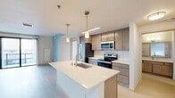 Located at 202 S Pinckney St in the heart of downtown Madison, Wisconsin, this modern one-bedroom, two-bathroom unit offers a well-designed single-floor layout with clean contemporary finishes throughout. The open-concept kitchen and living area serves as the centerpiece of the home, featuring a large quartz-topped island with an undermount sink and pendant lighting, light wood cabinetry, a subway tile backsplash, and a full suite of stainless steel appliances. Light wood-tone flooring runs through the kitchen and living areas, creating a warm, cohesive aesthetic. The living area is bright and open, with access to a private balcony through sliding glass doors that frame views of the surrounding Madison cityscape. A distinctive concrete column and ceiling fan add architectural character to the space. The primary bedroom is a comfortable size, also accessing the balcony via sliding doors and offering urban views. It features built-in closet shelving and connects to a dedicated bathroom. Both bathrooms are finished with clean white tile, light wood-tone flooring, dark-wood vanities, white quartz countertops, and tub-shower combinations. The overall ambiance is modern and minimal, with a neutral palette that creates a calm, functional living environment.