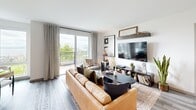 Located on the seventh floor in Seattle's Queen Anne neighborhood, this one-bedroom, one-bathroom residence offers a thoughtfully designed open-concept layout with modern finishes throughout. Light wood-tone flooring flows seamlessly across the living, dining, and kitchen areas, creating a cohesive and inviting atmosphere.

The kitchen is a standout feature, equipped with warm wood cabinetry, stainless steel appliances, a stone tile backsplash, and a large waterfall-edge peninsula with bar seating illuminated by sleek pendant lighting — ideal for both cooking and casual entertaining. The adjacent dining area benefits from a large picture window framing treetop and Puget Sound views, while the living room opens directly to a private balcony through sliding glass doors, extending the living space outdoors with panoramic water and city views.

The bedroom offers a serene retreat with a distinctive green accent wall, natural light from a large window, and a dedicated closet. In-unit laundry adds everyday convenience. The full bathroom features a tub-shower combination with matte black fixtures and clean white finishes. Throughout the residence, the design balances contemporary style with functional comfort, making this a well-appointed urban home in one of Seattle's most desirable neighborhoods.