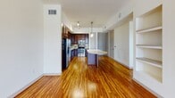 Located on Carlisle Street in Dallas, Texas, this single-floor residence presents a well-designed open layout with rich hardwood flooring that extends throughout the main living areas, reflecting light and adding warmth to the space. The open floor plan connects the living area seamlessly to the kitchen, creating a cohesive and functional environment.

The kitchen is a standout feature, showcasing rich dark mahogany cabinetry with glass-front upper panels, light stone countertops, and a mosaic tile backsplash in earthy tones. Stainless steel appliances, including a refrigerator, range, microwave, and dishwasher, complete the culinary space. A curved kitchen island provides additional prep and dining space.

The bedroom offers plush carpeting underfoot and features two windows with horizontal blinds that frame views of the surrounding Dallas cityscape, complemented by a ceiling fan for added comfort.

The bathroom includes large-format tile work and direct access to a spacious walk-in closet equipped with built-in shelving and racking systems, offering generous storage. Throughout the residence, white walls and clean lines contribute to a bright, modern aesthetic.
