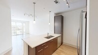 Located at 181 N. Pottstown Pike in Exton, PA, this thoughtfully designed one-bedroom, one-bathroom residence offers a clean, modern aesthetic throughout its efficiently organized single-floor layout. The open-concept living and kitchen area serves as the heart of the home, featuring light wood-toned flooring that flows seamlessly throughout the space. Large floor-to-ceiling windows and a glass sliding door flood the living area with natural light while providing views of the surrounding greenery, creating a bright and airy atmosphere. The kitchen is well-appointed with rich dark wood cabinetry, stainless steel appliances including a refrigerator, range, and microwave, and a sleek white countertop island with a built-in sink. Stylish pendant lighting and track fixtures add a contemporary touch overhead. The bedroom is a comfortable retreat, finished with plush carpeting, a ceiling fan, and a window fitted with blinds that invite natural light. The bathroom continues the modern design language with dark wood vanity cabinetry, a white countertop, a large mirror, and a tub-shower combination with tile surround. Neutral tones and clean lines throughout give this residence a fresh, move-in-ready appeal.