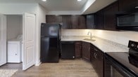 This two-floor residence offers a thoughtfully designed layout with a clean, neutral aesthetic throughout. The kitchen serves as a standout feature, outfitted with rich dark espresso cabinetry, granite-style countertops, and a full suite of black appliances including a refrigerator, electric range, built-in microwave, and dishwasher. Wood-look flooring ties the kitchen together, lending a warm, contemporary feel to the space.

The bedrooms are generously proportioned, each featuring soft wall-to-wall carpeting in a neutral tan tone, crisp white walls, and clean panel doors. Natural light filters in through window blinds, creating a bright and inviting atmosphere. The rooms offer a versatile, open canvas suitable for a variety of layouts and uses.

The bathrooms are finished with a consistent design language — dark-stained vanity cabinetry paired with white countertops, tile flooring, and chrome fixtures. One bathroom includes a full tub-shower combination with subway tile surround, while another features a half-bath configuration with chrome accessory bars and wood-look flooring. Recessed lighting and mirrored vanities add functionality and polish. Overall, the space presents a modern, move-in ready environment with cohesive finishes across both floors.