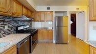 Located at 39 Village Ct in Boston's South End neighborhood, this two-floor residence offers a functional and well-appointed layout across both levels. Light-toned hardwood flooring runs throughout, lending a clean, cohesive look to every room.

The kitchen is a standout feature, outfitted with warm oak cabinetry, granite countertops, a decorative mosaic tile backsplash, and a full suite of stainless steel appliances including a gas range, dishwasher, and refrigerator. A dedicated under-cabinet range hood adds to its practical design.

The living area on the lower level is open and well-lit, with large windows allowing natural light to fill the space. A dark-toned staircase connects to the upper floor, where multiple bedrooms are found. Each bedroom features the same hardwood flooring, neutral walls, and windows with outdoor views of surrounding greenery. At least one bedroom includes a sliding-door closet with built-in shelving. An additional flexible lower-level room with wall-mounted climate control provides versatile space for various uses.

The bathroom is cleanly finished in white tile, featuring a full soaking tub with shower, a pedestal sink, and a wall-mounted mirror. The overall ambiance is bright, neutral, and move-in ready.