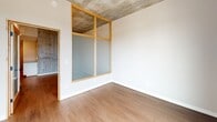 Located at 127 N 17th St in Richmond, VA, this one-bedroom, one-bathroom unit offers a thoughtfully designed layout that blends modern finishes with industrial architectural character. The space is defined by striking exposed concrete ceilings throughout, which lend a raw, urban aesthetic that contrasts beautifully with the clean white walls and warm hardwood-style flooring.

The kitchen is a standout feature, designed in a galley configuration with white shaker cabinetry, granite countertops, a subway tile backsplash, and stainless steel appliances. An exposed concrete accent wall adds industrial texture alongside the sleek, functional workspace.

The spacious bedroom is among the most distinctive areas of the unit, featuring a floor-to-ceiling glass partition with warm wood framing that allows light to filter through while maintaining a sense of separation. The exposed concrete ceiling continues here, reinforcing the loft-like character of the space.

Interior doors are fitted with frosted glass panels and natural wood frames, maintaining privacy while allowing light to flow throughout. Wall sconces provide warm ambient lighting in the entryway and bedroom areas.

The bathroom is clean and functional, featuring a full tub-shower combination, tile flooring, granite vanity surface, and brushed nickel fixtures and towel bars. The overall ambiance of the unit is modern and urban, with industrial-chic details that make it a distinctive offering in Richmond's downtown corridor.