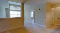 This single-floor residence offers a clean, functional layout designed with comfort and connectivity in mind. The main living area is finished with warm hardwood flooring that adds a classic touch to the open space. Neutral, light-toned walls create a calm and welcoming ambiance throughout, while large windows fitted with horizontal blinds allow generous amounts of natural light to fill the rooms.

A ceiling fan is positioned in the living area, contributing both to the aesthetic and to everyday comfort. Wide doorways connect the spaces, allowing natural sightlines from room to room and reinforcing the open, airy feel of the floor plan. Adjacent rooms feature plush carpeting, offering a comfortable contrast to the hardwood in the main area.

White-painted trim and baseboards provide a crisp, finished look along the walls and doorframes, lending a sense of polish to the interior. A fire safety device is mounted on the wall, reflecting attention to safety standards within the space. The layout flows naturally between areas, with well-placed windows ensuring that even interior-facing rooms benefit from borrowed natural light. Overall, this residence presents a straightforward, move-in-ready environment with a bright, neutral palette suitable for a variety of uses and personal styles.