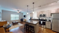 Located at 8931 N Montgall Ave in Kansas City, Missouri, this single-floor residence offers a well-designed open-concept layout that seamlessly connects the kitchen and living areas. The kitchen is equipped with stainless steel appliances — including a range, microwave, dishwasher, and refrigerator — complemented by light wood cabinetry, dark granite countertops, a center island with bar seating, and pendant lighting. Track lighting and crown molding add a polished finish to the space. The living room features rich hardwood flooring, crown molding, a ceiling fan, and windows that invite natural light. A secondary sitting area provides additional living space with the same warm aesthetic. The primary bedroom offers plush carpeting, a ceiling fan, and direct access to a full en-suite bathroom featuring a double-sink vanity with dark granite countertops, light wood cabinetry, and a shower-tub combination. A second bedroom is similarly bright and carpeted with natural light from a large window. A powder room with a pedestal sink and hardwood flooring serves as a convenient half bath. Throughout the home, neutral tones, consistent finishes, and thoughtful detailing create a cohesive and comfortable living environment.
