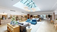 This single-floor facility makes a strong first impression with its expansive central lobby, where a dramatic pyramid skylight floods the polished concrete floors with natural light. Suspended woven pendant chandeliers add warmth to the bright, open atmosphere, while the high ceilings amplify the sense of spaciousness. The lobby is furnished with a curated mix of coastal-inspired seating, rattan-accented consoles, and lush potted greenery, creating an inviting and refined ambiance. Entry is accessible via a grand staircase flanked by metal railings.

Adjacent to the lobby, a large conference room accommodates sizeable gatherings around a long wooden table with upholstered blue chairs. A wide interior window connects this room to the main lobby, maintaining visual openness throughout the space.

Corridors extend from the lobby with warm wainscoting, art-adorned walls, and thoughtfully placed seating vignettes that contribute to the welcoming character of the space. Elevator lobbies feature textured wallcoverings, polished concrete floors, and a curated lounge chair, offering a refined transitional experience.

The building also includes a dedicated, well-organized bike storage area with wall-mounted racks lining painted concrete block walls — a practical amenity for active occupants.