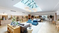 This single-floor facility makes a strong first impression with its expansive central lobby, where a dramatic pyramid skylight floods the polished concrete floors with natural light. Suspended woven pendant chandeliers add warmth to the bright, open atmosphere, while the high ceilings amplify the sense of spaciousness. The lobby is furnished with a curated mix of coastal-inspired seating, rattan-accented consoles, and lush potted greenery, creating an inviting and refined ambiance. Entry is accessible via a grand staircase flanked by metal railings.

Adjacent to the lobby, a large conference room accommodates sizeable gatherings around a long wooden table with upholstered blue chairs. A wide interior window connects this room to the main lobby, maintaining visual openness throughout the space.

Corridors extend from the lobby with warm wainscoting, art-adorned walls, and thoughtfully placed seating vignettes that contribute to the welcoming character of the space. Elevator lobbies feature textured wallcoverings, polished concrete floors, and a curated lounge chair, offering a refined transitional experience.

The building also includes a dedicated, well-organized bike storage area with wall-mounted racks lining painted concrete block walls — a practical amenity for active occupants.