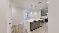 Located at 510 McLean St in Belmont, NC, this well-appointed residence offers four bedrooms and two full bathrooms across a single floor. The open-concept kitchen and living area serves as the heart of the home, anchored by a central island with a built-in sink, pendant lighting, and crisp white countertops. Gray shaker-style cabinetry pairs seamlessly with a full suite of stainless steel appliances, including a French door refrigerator, range, microwave, and dishwasher. Light wood-look luxury vinyl plank flooring extends throughout the entire home, creating a cohesive and easy-to-maintain aesthetic. The living area benefits from natural light through a large window and direct access to an outdoor balcony. The four bedrooms offer comfortable proportions, with the primary bedroom featuring a ceiling fan and a walk-in closet equipped with built-in wire shelving. The primary bathroom includes a dual-sink vanity with gray cabinetry and a glass-enclosed shower, while the second bathroom features a full tub-shower combination with matching finishes. Neutral wall tones and recessed lighting throughout contribute to a clean, modern ambiance well suited for everyday living.