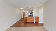 This single-floor unit offers a thoughtfully designed layout with distinct living, sleeping, and functional zones. The kitchen serves as a central highlight, featuring warm honey-toned wood cabinetry, granite countertops, and a full suite of stainless steel appliances including a refrigerator, range, microwave, and dishwasher. A subway tile backsplash adds a clean, classic detail, while rich hardwood flooring grounds the space. A granite-topped peninsula provides additional prep and seating space and opens toward the living area, which transitions to plush wall-to-wall carpeting. The living area benefits from multiple windows fitted with horizontal blinds, allowing natural light to filter throughout. Bedroom spaces are carpeted and feature textured ceilings and windows that bring in additional daylight. Two bathrooms are present, each finished with light tile flooring and rich wood vanities topped with white countertops. One bathroom includes ADA-compliant grab bars, reflecting a practical and inclusive design approach. The overall aesthetic is neutral and cohesive, with soft gray and beige tones throughout.