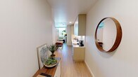 Located at 1734 Webster St in Oakland's vibrant Uptown district, this single-floor studio unit offers a thoughtfully designed open-concept layout that maximizes every inch of space. Light wood flooring runs throughout, complementing the clean white walls and striking exposed concrete ceilings that lend an industrial-modern character to the interior.

The galley-style kitchen is outfitted with floor-to-ceiling light wood cabinetry, under-cabinet lighting, a white countertop, stainless steel sink, electric cooktop, and a built-in oven — providing full cooking functionality in a compact, efficient footprint. A small dining area sits adjacent, ideal for casual meals.

A freestanding partition wall elegantly divides the sleeping area from the rest of the unit, creating a sense of privacy around the bed without fully closing off the space. The living area accommodates a sofa and features a bright, airy window that draws natural light into the room, enhancing the open ambiance.

The bathroom is clean and modern, featuring a wall-mounted vanity with a white countertop, large mirror, and simple, understated finishes. Tasteful artwork and potted greenery are placed throughout the unit, adding warmth and a personal touch to the minimalist aesthetic. The overall design reflects a practical yet stylish approach well-suited to urban living in Oakland.