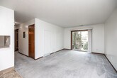 Located in West Des Moines, Iowa, this one-bedroom, one-bathroom unit offers a practical and well-organized single-floor layout. The living room is the heart of the space, featuring soft carpeted flooring, warm wood baseboards, and a textured ceiling. A large sliding glass door floods the room with natural light and opens to a private balcony with outdoor views, creating a bright and airy atmosphere. A ceiling fan with light fixture adds both function and comfort to the space. The kitchen is positioned adjacent to the living area, separated by a convenient pass-through counter. It features tile flooring, warm wood cabinetry, a white appliance suite including a stove and refrigerator, and a sink with views into the main living space. A hallway connects the main areas and leads to the bedroom and bathroom. The bedroom is a comfortable, carpeted retreat with a ceiling fan, a window that brings in natural light, and a reach-in closet with a full-length hanging rod and shelf for organized storage. The bathroom is clean and functional, featuring tile flooring and a shower/tub combination. Throughout the unit, consistent warm wood trim and doors tie the design together, creating a cohesive and inviting feel.