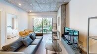 This contemporary 810 square foot apartment offers a harmonious blend of industrial chic and modern comfort. The open-concept layout maximizes space, seamlessly integrating the kitchen, living, and dining areas. The kitchen boasts sleek cabinetry, stainless steel appliances, and under-cabinet lighting, creating a sophisticated cooking environment.

The living area is bathed in natural light from large windows, which also provide verdant views of surrounding greenery. Concrete ceilings add an industrial touch, while warm wood flooring softens the aesthetic. A stylish entertainment center and comfortable seating create an inviting atmosphere for relaxation or socializing.

Both bedrooms feature ample space, with the primary bedroom measuring 120 square feet. Large windows in the bedrooms offer abundant natural light and scenic views. Built-in wooden wardrobes provide generous storage solutions.

The bathrooms are designed with modern fixtures, including glass-enclosed showers, illuminated mirrors, and sleek vanities. The apartment's hallway efficiently connects all spaces, with a convenient closet for additional storage.

Throughout the apartment, the interplay of textures—concrete, wood, and glass—creates a visually interesting and cohesive design. This TENTEN Downtown residence perfectly balances urban sophistication with functional living space.
