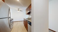 This single-floor, one-bedroom, one-bathroom unit offers a practical and comfortable layout across a well-utilized footprint. The galley-style kitchen is a functional highlight, featuring rich warm-toned wood cabinetry, granite countertops, stainless steel appliances including a range, microwave, and refrigerator, and light wood-look flooring that extends throughout the space. A dedicated sink area with additional cabinetry provides ample storage and prep space.

The living room is a bright and open area anchored by a sliding glass door that leads to a private balcony, offering views of mature trees and the surrounding landscape. Carpet flooring, a ceiling fan with integrated lighting, a wall-mounted air conditioning unit, and baseboard heating make this room versatile across seasons.

The bedroom is a generously sized retreat, featuring plush carpet flooring, a window with outdoor views, baseboard heating, and a closet. The bathroom includes a full tub and shower combination with tile surround, a grab bar, tile flooring, and a wood-toned vanity with a dark countertop. The overall ambiance of the unit is clean, neutral, and functional.