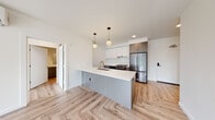 Located at 4055 Mercantile Dr in Lake Oswego, Oregon, this thoughtfully designed single-floor residence showcases contemporary finishes and a clean, modern aesthetic throughout. The open-concept kitchen serves as the heart of the home, featuring a large waterfall-edge island with an undermount sink and brushed gold faucet, quartz countertops, a subway tile backsplash, two-tone cabinetry in white and charcoal gray, and premium stainless steel appliances including a gas range and a full-size refrigerator. Globe pendant lights add a refined touch overhead. The kitchen flows seamlessly into the living area, which is bathed in natural light from large windows offering views of the surrounding neighborhood. A wall-mounted mini-split system provides efficient climate control throughout. Luxury herringbone-patterned hardwood flooring runs throughout the space, adding warmth and visual interest. The bedrooms are bright and well-proportioned, with generous windows and clean white walls. The primary bathroom features a dual-sink vanity with charcoal cabinetry, white quartz countertops, wall-mounted sconce lighting, and a glass-enclosed shower. A secondary bathroom offers a soaking tub with a rain showerhead and vertical subway tile surround. In-unit laundry facilities are also present, adding everyday convenience to this polished Lake Oswego residence.