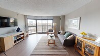 Situated along North Clark Street in Chicago's vibrant Lincoln Park neighborhood, this single-floor residence offers a well-designed layout with a cohesive, neutral aesthetic throughout. The expansive living area is the centerpiece of the space, featuring warm hardwood-style flooring, a textured ceiling, and floor-to-ceiling windows that flood the room with natural light and frame panoramic views of the surrounding cityscape. A sliding glass door provides access to a private balcony, extending the living space outdoors. The living room flows seamlessly into a dining area, where additional windows continue to bring in natural light and urban views, creating a bright and airy atmosphere. The kitchen is outfitted with white shaker-style cabinetry, dark countertops, a gray tile backsplash, and a stainless steel sink, offering a clean and functional workspace. The bedroom is carpeted for comfort and benefits from large windows that allow natural light to filter in, complemented by soft, neutral-toned walls. The bathroom features white tile flooring, a combination tub and shower, and white vanity cabinetry with matching countertops, maintaining the clean and understated palette found throughout the residence. Overall, the space presents a modern, comfortable environment with consistent finishes and excellent access to natural light and city views.