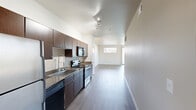 Located in Austin's vibrant Domain neighborhood, this one-bedroom, one-bathroom residence offers a thoughtfully designed open-concept layout with modern finishes throughout. The combined kitchen and living area forms the heart of the space, featuring wood-look plank flooring that flows seamlessly underfoot. The kitchen is well-appointed with rich dark wood cabinetry, granite countertops, a subway tile backsplash, stainless steel appliances including a range and refrigerator, and track lighting overhead. The living room is bright and airy, benefiting from a large sliding glass door that opens to a private balcony offering open views of the surrounding neighborhood, complemented by an additional horizontal accent window that brings in extra natural light. The bedroom is carpeted for comfort and connects directly to a dedicated walk-in closet with built-in shelving and hanging rods. The full bathroom features tile flooring, a dual-sink vanity with granite countertops and vessel sinks, warm wood cabinetry, and a tub-shower combination with tiled surround. Neutral wall tones and clean architectural lines throughout lend the space a cohesive, contemporary feel.
