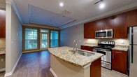 Located on Northlake Parkway Northeast in Atlanta, GA, this well-appointed one-bedroom, one-bathroom residence offers a thoughtfully designed single-level layout. The open-concept kitchen and living area serves as the heart of the home, anchored by a granite-topped kitchen island with an integrated sink. Rich cherry wood cabinetry reaches toward the ceiling, complemented by stainless steel appliances including a refrigerator, electric range, and built-in microwave. Hardwood-style flooring runs throughout the main living area, which features crown molding and a tray ceiling detail that adds architectural character. A full glass-paned door flanked by large windows floods the living space with natural light and provides outdoor access. The bedroom is a comfortable retreat with dark hardwood-style floors, a ceiling fan, and a window with exterior views. It connects directly to the full bathroom, which features a cherry wood vanity, framed mirror, and light tile flooring. A dedicated laundry room with full-size washer and dryer hookups and overhead shelving adds everyday convenience. A separate closet provides additional storage, completing this efficiently laid-out and well-finished residence.