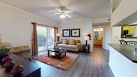 This well-appointed single-floor residence at 9451 Welby Rd in Thornton, Colorado offers a cohesive and functional layout designed for comfortable everyday living. The living room serves as the heart of the home, featuring rich hardwood-style flooring, crown molding, and a ceiling fan that adds both style and practicality. Large sliding glass doors flood the space with natural light and open directly onto a private balcony overlooking lush greenery, creating a seamless indoor-outdoor connection. The open layout connects the living area to the kitchen via a pass-through counter, providing an easy flow between spaces. The galley-style kitchen is efficiently designed with bold yellow cabinetry, black appliances including a refrigerator, range, and dishwasher, dark countertops, and a double sink — offering everything needed for daily meal preparation. The bedroom is a calm retreat, featuring plush carpeting, generous natural light through a large window with striped drapery, and wall-mounted shelving for added storage. The bathroom includes a full tub-shower combo with tiled surround and is conveniently adjacent to a spacious walk-in closet with built-in shelving and hanging rods. Throughout the residence, neutral tones and warm accents create an inviting and cohesive ambiance.