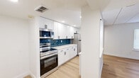 Located at 8216 Frankford Ave in the Holmesburg neighborhood of Philadelphia, PA, this fully renovated single-floor unit showcases a clean, contemporary design with bright white walls, light hardwood flooring, and recessed lighting throughout. The open-concept layout connects a spacious living area to a well-appointed kitchen, which serves as the centerpiece of the unit. The kitchen features crisp white shaker-style cabinetry, sleek quartz countertops, a striking deep-blue herringbone tile backsplash, and a full suite of stainless steel appliances including a range, over-the-range microwave, and refrigerator. A peninsula with pendant lighting creates a natural divide between the kitchen and living space, enhancing both function and flow. The living area is generously proportioned, with paneled ceilings and direct sightlines into the kitchen. The bedrooms are bright and well-sized, each benefiting from natural light through window blinds and light hardwood floors. One bedroom notably features dual sliding closets, providing substantial built-in storage. The bathroom is finished with bold teal subway tile surrounding a full soaking tub and shower combination, complemented by matte black hardware and neutral tile flooring. The unit presents a cohesive, modern aesthetic throughout, with consistent design details tying every room together.