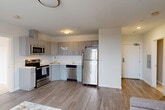 This 2-bedroom, 2-bathroom residence in Boston, MA offers a thoughtfully designed single-floor layout that maximizes functionality and comfort. The open-concept living, dining, and kitchen area serves as the heart of the home, bathed in natural light from large double-hung windows. The kitchen features sleek, high-gloss gray cabinetry, white countertops, and a full suite of stainless steel appliances including a refrigerator, range, microwave, and dishwasher, all set atop durable wood-look flooring. The combined living and dining space provides a bright, airy atmosphere with clean white walls and a neutral palette throughout. The primary bedroom is a comfortable retreat with plush carpeting, two windows offering outdoor views, and access to a dedicated closet. The second bedroom mirrors this warmth with its own natural light and closet space. Both bathrooms are cleanly finished with tile flooring, vanities, and shower enclosures. Additional highlights include three closets for generous storage, an in-unit laundry area, and a consistent modern aesthetic carried throughout. The crisp white walls, contemporary fixtures, and thoughtful layout make this a well-appointed Boston residence.