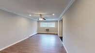 Located at Fairfield North at Patchogue in East Patchogue, New York, this single-floor residence offers a clean, modern aesthetic defined by consistent hardwood-style flooring, crisp crown molding, and neutral gray walls that flow seamlessly throughout the home. Recessed lighting illuminates the open hallway and living areas, complementing the bright, airy atmosphere created by natural light filtering through multiple windows.

The spacious living area features a ceiling fan with integrated lighting, a wall-mounted air conditioning unit, and baseboard heating, ensuring year-round comfort. Crown molding frames the ceiling elegantly, adding a refined architectural detail to the room.

The kitchen is a standout feature, showcasing rich cherry wood cabinetry, dark granite countertops, a granite tile backsplash, and polished dark tile flooring. Stainless steel appliances, including a refrigerator, dishwasher, and range with microwave, complete this well-equipped space.

Bedroom areas continue the hardwood-style flooring and crown molding theme, with sliding panel closets offering generous storage. The bathroom includes a tub-shower combination enclosed by sliding glass doors, accented with white tile and decorative diamond inlays and chrome fixtures, providing a clean, polished finish.