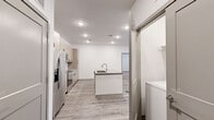 This well-appointed 2-bedroom, 2-bathroom single-story unit offers a thoughtfully designed open-concept layout. The kitchen and living area flow seamlessly together, anchored by a central island with an integrated sink and light gray countertops. The kitchen is equipped with stainless steel appliances — including a French door refrigerator, electric range, and over-the-range microwave — complemented by light wood cabinetry with matte black hardware and a classic white subway tile backsplash. Light-tone wood-look flooring runs throughout the main living areas, adding warmth and continuity.

The spacious living room features a ceiling fan and a window allowing for natural light. Both bedrooms are carpeted for comfort and include ceiling fans and dedicated walk-in closets with built-in shelving and hanging rods. The primary bedroom offers a comfortable footprint with direct access to its closet.

Each bathroom is finished with light wood vanity cabinetry, gray quartz countertops, matte black fixtures, and wood-look flooring. One bathroom includes a soaking tub with a shower surround. A hallway connects the private areas of the unit, and in-unit laundry hookups are conveniently located near the kitchen. The overall design is clean, modern, and move-in ready.