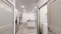 This well-appointed 2-bedroom, 2-bathroom single-story unit offers a thoughtfully designed open-concept layout. The kitchen and living area flow seamlessly together, anchored by a central island with an integrated sink and light gray countertops. The kitchen is equipped with stainless steel appliances — including a French door refrigerator, electric range, and over-the-range microwave — complemented by light wood cabinetry with matte black hardware and a classic white subway tile backsplash. Light-tone wood-look flooring runs throughout the main living areas, adding warmth and continuity.

The spacious living room features a ceiling fan and a window allowing for natural light. Both bedrooms are carpeted for comfort and include ceiling fans and dedicated walk-in closets with built-in shelving and hanging rods. The primary bedroom offers a comfortable footprint with direct access to its closet.

Each bathroom is finished with light wood vanity cabinetry, gray quartz countertops, matte black fixtures, and wood-look flooring. One bathroom includes a soaking tub with a shower surround. A hallway connects the private areas of the unit, and in-unit laundry hookups are conveniently located near the kitchen. The overall design is clean, modern, and move-in ready.