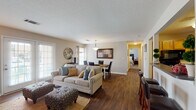 This single-floor residence offers a thoughtfully designed open-concept layout that seamlessly connects the living, dining, and kitchen areas. Rich, dark hardwood-style flooring extends throughout the main living spaces, adding warmth and continuity to the design.

The living room is generously proportioned, featuring neutral-toned walls, a textured ceiling, and large windows with blinds that invite natural light. French doors open to the exterior, providing additional brightness and outdoor access. The dining area sits adjacent to the living room, illuminated by a pendant light fixture and framed by a large window, creating an inviting setting for meals.

The kitchen is well-appointed with warm wood cabinetry, dark countertops, black appliances, and a double basin sink. A breakfast bar with seating offers a casual dining option and connects the kitchen to the main living area.

The bedroom is a comfortable retreat featuring plush carpet, a ceiling fan, and neutral walls that create a calm atmosphere. The bathroom includes a full tub-shower combination with clean white tile surroundings.

A dedicated in-unit laundry room houses a full-size washer and dryer set alongside overhead wire shelving, adding practical convenience. Throughout the space, the consistent use of neutral tones and natural materials creates a cohesive and welcoming ambiance.