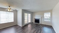 This single-floor, 2-bedroom, 2-bathroom residence offers a well-considered layout designed for comfortable everyday living. The main living area serves as the heart of the home, featuring dark hardwood-style flooring that runs throughout and provides a warm, grounding contrast to the light neutral-toned walls. A white-mantled fireplace with tile surround anchors the living space, adding both a functional and aesthetic focal point. Natural light fills the room through multiple windows and a set of classic French doors, which open to the outdoors and enhance the sense of openness. The textured ceiling adds a traditional architectural finish consistent throughout the space. The living area flows naturally into the rest of the home, connecting to the two bedrooms and two full bathrooms that complete this residence. With its combination of a wood-look floor, fireplace, and French door access, this home balances practicality with inviting design elements. The layout makes efficient use of its footprint, providing distinct living zones within a single-story format that is easy to navigate and maintain.