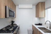 Located in the Westwood neighborhood of Los Angeles, this single-floor unit at 1629 Veteran Ave showcases a thoughtfully designed modern interior with a clean, minimalist aesthetic throughout. Light wood-tone flooring runs seamlessly across the living areas, complementing the warm natural wood cabinetry that defines the space's character.

The main living area features a built-in wall unit with ample upper and lower cabinetry in a light oak finish, a wall-mounted flat-screen television, and a white countertop surface that provides both functionality and visual continuity. A keypad-secured entry door opens directly into this well-organized space, which also accommodates a comfortable seating area.

The sleeping area is compact yet functional, furnished with a bed, bedside lighting, a small dining table with chairs, and a wall-mounted split air conditioning unit for year-round climate control. Contemporary artwork adds a pop of color to the crisp white walls.

The bathroom is finished to a high standard, featuring large-format porcelain tile flooring and wall tiling, a frameless glass-enclosed walk-in shower with a window for natural light, and a floating vanity with warm wood cabinetry, white quartz countertop, an undermount sink, and a large backlit mirror. Chrome fixtures throughout add a polished, cohesive finishing touch to the space.