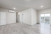 This single-floor unit offers a clean, contemporary design with a neutral color palette of warm beige and soft white throughout. Light wood-look luxury vinyl plank flooring extends across the living areas and bedrooms, complementing the smooth, light gray baseboards and recessed lighting overhead.

The open living area is generously proportioned, providing ample space for comfortable furnishing arrangements. A wall-mounted mini-split HVAC unit ensures efficient climate control. The layout connects seamlessly to a well-appointed kitchen featuring white shaker-style cabinetry, gray laminate countertops, a stainless steel dishwasher, electric range, over-the-range microwave, and a double-basin sink. A door from the kitchen provides access to an outdoor area.

The bedrooms are comfortably sized, with one room benefiting from a window that brings in natural light. An electrical panel is conveniently located near the main living space. The bathrooms are finished with large-format marble-look ceramic tile surrounding full soaking tub and shower combinations, paired with chrome fixtures, offering a clean and polished aesthetic throughout.