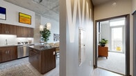 This contemporary 2-bedroom, 1-bathroom residence showcases a striking industrial-chic aesthetic defined by soaring exposed concrete ceilings, light wood-toned flooring, and an open, airy layout. The combined kitchen and living area serves as the heart of the home, where a well-appointed kitchen impresses with rich dark wood cabinetry, stainless steel appliances, a mosaic tile backsplash, quartz countertops, and a central island with pendant lighting overhead. The living room flows naturally from the kitchen, bathed in natural light from floor-to-ceiling windows that frame urban skyline views and open to a private balcony. The primary bedroom continues the modern theme with high ceilings, large sliding glass doors accessing the balcony, soft carpeting, and a dedicated walk-in closet offering generous storage. The second bedroom is equally well-proportioned and bright. The bathroom features a frameless glass walk-in shower with clean white tile surround, a dark wood vanity, and elegant stone-look tile flooring. Throughout the residence, thoughtful architectural details — including exposed concrete columns and high ceilings — lend a distinct urban character, creating a refined yet comfortable living environment.