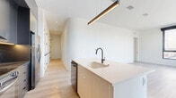Located at 1111 Fairfield Avenue in Cleveland's 44113 zip code, this modern two-bedroom, two-bathroom residence offers a thoughtfully designed single-floor layout with clean, contemporary finishes throughout. Light-toned hardwood flooring flows seamlessly across every room, complementing the crisp white walls and creating a bright, cohesive aesthetic.

The open-concept kitchen and living area serves as the heart of the home. The kitchen features a sleek center island with an undermount sink and matte black faucet, warm-toned flat-front cabinetry, dark upper cabinets with under-cabinet lighting, a tile backsplash, stainless steel appliances, and a built-in dishwasher. A linear pendant light fixture anchors the island, while a large black-framed window floods the space with natural light.

A wide hallway connects the living areas to the two bedrooms, lined with flush-panel doors with matte black hardware. The generously sized primary bedroom features floor-to-ceiling black-framed windows offering neighborhood views, built-in closet organizers with dedicated shelving and drawers, and ample space. The second bedroom also benefits from large windows and abundant natural light.

Both bathrooms are finished in a modern style, with one featuring full-height stacked tile surrounding a soaking tub, a wall-mounted vanity, an illuminated mirror, and matte black fixtures throughout.
