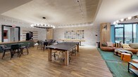 This single-floor community and amenity space showcases a thoughtfully designed interior that merges industrial aesthetics with warm, rustic character. Polished concrete and rich hardwood flooring run throughout, complemented by exposed brick walls, wood-paneled accents, and steel-framed glass partitions that define zones while maintaining an open, connected feel. Large black-steel garage-style doors open directly to an outdoor patio, flooding the interior with natural light and creating a seamless indoor-outdoor connection.

The main lounge area features built-in bookshelves, a bold Michigan-themed mural, and a mix of leather sofas, round café tables, and bar-height seating arranged around a central fireplace. A dedicated games area includes a ping pong table, shuffleboard, and a pool table, all set beneath industrial track and pendant lighting. A glass-enclosed conference or meeting room with a reclaimed wood sliding barn door provides a more private setting for gatherings or work sessions.

A cozy media lounge offers tufted leather chesterfield sofas, a wood-paneled ceiling, and multiple large-screen televisions, creating an intimate viewing environment. The entire space is unified by consistent use of natural wood tones, black metal fixtures, and purposeful, community-oriented design throughout.