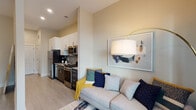Located at 530 N Patterson Ave in Winston-Salem, NC, this single-floor unit offers a well-designed open-concept layout that seamlessly integrates the living and kitchen areas. The kitchen is outfitted with stainless steel appliances, including a refrigerator, range, microwave, and dishwasher, complemented by sleek white upper cabinetry, dark lower cabinets, granite countertops, and a tile backsplash. Light wood-tone flooring runs throughout, creating a cohesive and contemporary aesthetic. The living area is bright and welcoming, featuring large windows that invite natural light and offer views of the surrounding neighborhood. The space accommodates a comfortable seating area with room for a full media setup along the wall. A dedicated walk-in closet provides generous storage with wire shelving systems and ample floor space. The bathroom includes a full tub and shower combination, granite vanity countertop, dark cabinetry, and wood-tone tile flooring. A stacked in-unit washer and dryer adds everyday convenience. Neutral wall tones and recessed lighting throughout contribute to a clean, modern ambiance suited for efficient urban living.