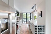 Located in Washington, DC's vibrant Shaw neighborhood, this well-appointed 2-bedroom, 2-bathroom residence offers a thoughtfully designed single-level layout. The entrance hallway, finished with warm hardwood flooring and adorned with patterned runner rugs, leads seamlessly into the heart of the home. The open-concept kitchen is a standout feature, boasting floor-to-ceiling windows, sleek gray cabinetry, white subway tile backsplash, stainless steel appliances, a built-in wine rack, and a quartz waterfall island illuminated by stylish globe pendant lights. A sliding glass door opens directly onto a private balcony, flooding the space with natural light and outdoor views. The combined dining and living area is bright and airy, highlighted by light hardwood floors and a charming arched alcove detail. Both bedrooms are comfortably sized, each featuring warm terracotta accent walls, built-in closets, and large windows. The primary bathroom offers a spacious glass-enclosed walk-in shower with large-format white tile and a teak bench, while the second bathroom includes a modern vanity with a vessel sink and a tub-shower combination. A dedicated laundry area and four closets round out this efficiently organized and stylishly finished residence.