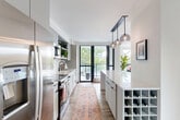 Located in Washington, DC's vibrant Shaw neighborhood, this well-appointed 2-bedroom, 2-bathroom residence offers a thoughtfully designed single-level layout. The entrance hallway, finished with warm hardwood flooring and adorned with patterned runner rugs, leads seamlessly into the heart of the home. The open-concept kitchen is a standout feature, boasting floor-to-ceiling windows, sleek gray cabinetry, white subway tile backsplash, stainless steel appliances, a built-in wine rack, and a quartz waterfall island illuminated by stylish globe pendant lights. A sliding glass door opens directly onto a private balcony, flooding the space with natural light and outdoor views. The combined dining and living area is bright and airy, highlighted by light hardwood floors and a charming arched alcove detail. Both bedrooms are comfortably sized, each featuring warm terracotta accent walls, built-in closets, and large windows. The primary bathroom offers a spacious glass-enclosed walk-in shower with large-format white tile and a teak bench, while the second bathroom includes a modern vanity with a vessel sink and a tub-shower combination. A dedicated laundry area and four closets round out this efficiently organized and stylishly finished residence.