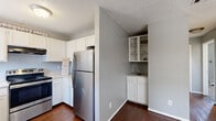 This single-floor, 2-bedroom, 1-bathroom unit offers an efficient and well-organized layout designed to maximize its compact footprint. The kitchen is a functional highlight, featuring white cabinetry, light countertops, stainless steel appliances including a refrigerator and electric range, and a double basin sink beneath a window that allows natural light to filter in. A built-in shelving nook with white cabinetry adjacent to the kitchen provides additional storage and display space. Rich, dark hardwood-style flooring runs throughout the kitchen and hallway areas, creating a warm contrast against the soft gray walls.

A central hallway connects the main living areas to the two bedrooms and shared bathroom, offering a clean and logical flow through the unit. Both bedrooms feature plush carpeting and neutral gray walls, with the primary bedroom offering a notably more spacious feel. A textured ceiling is consistent throughout the unit. The shared bathroom is accessible from the hallway and includes a white vanity. A dedicated closet provides added storage convenience. The overall design palette of white trim, gray walls, and mixed flooring gives the space a clean, neutral, and move-in-ready aesthetic.