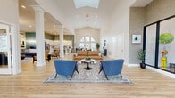 Located in Hebron, Kentucky, this single-floor leasing office for an apartment community offers a generously sized, open-plan interior designed to impress and inform prospective residents. The space is anchored by a dramatic vaulted ceiling with a skylight, flooding the main lounge area with natural light. A grand arched window at the entrance adds architectural character, framing views of the surrounding landscape and creating a welcoming first impression. Light-toned hardwood-style flooring runs throughout, unifying the various functional zones seamlessly.

The reception area features a clean, white credenza-style desk, offering a professional yet approachable welcome point. Adjacent to it, a glass-enclosed consultation room with black-framed partitions provides a dedicated space for private leasing discussions, complete with pendant lighting and a round meeting table. Bold, botanical-print wallcoverings add a vibrant, artistic touch throughout the space.

The fully equipped demonstration kitchen stands out with white shaker cabinetry, a herringbone-patterned island clad in reclaimed wood-look panels, stainless steel appliances, and sculptural gold pendant lighting. Bar-height seating along the island encourages casual interaction. The open lounge area is thoughtfully furnished with comfortable seating arrangements, completing this welcoming, well-appointed leasing environment.