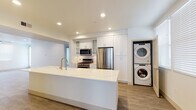 Located at 6720 Calle Koral in Goleta, California, this single-story residence showcases a clean, modern design with an open and airy layout. The heart of the home is a well-appointed kitchen featuring a large center island with a quartz waterfall countertop, a brushed gold faucet, and generous prep space. White shaker-style cabinetry with glass-front upper cabinets extends floor to ceiling, complemented by stainless steel appliances including a gas range, built-in microwave, and a French door refrigerator. A stacked washer and dryer unit is conveniently integrated into the kitchen area. Light wood-tone flooring flows throughout the main living spaces, lending warmth and continuity to the open floor plan. The spacious living area is bright and welcoming, enhanced by recessed lighting and a ceiling fan. Bedrooms feature plush carpeting, ceiling fans, and windows with blinds that allow for natural light. The bathroom is finished with a dual-sink vanity topped in quartz, white shaker cabinetry with brushed nickel hardware, and a large mirror. The overall aesthetic is modern and neutral, offering a clean, move-in-ready environment in the desirable Goleta community.