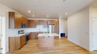 This well-appointed 2-bedroom, 2-bathroom unit offers a practical and modern layout across a single floor. The open-concept kitchen and living area serves as the heart of the home, showcasing warm wood-toned cabinetry that extends to the ceiling for ample storage, complemented by a white subway tile backsplash and crisp white quartz countertops. A central kitchen island provides additional workspace and casual seating, while stainless steel appliances — including a refrigerator, range, and microwave — complete the contemporary look. Light wood-style flooring flows throughout the main living areas, adding warmth and continuity to the space.

The primary bedroom is generously sized, featuring a ceiling fan, light-filtering window treatments, and direct access to a private bathroom. The second bedroom is carpeted, bright, and equipped with a ceiling fan and window for natural light. A hallway connects the bedrooms to the bathrooms, one of which includes a full soaking tub and shower combination with clean white surrounds and wood-toned vanity cabinetry. A dedicated closet provides additional storage. The unit's clean, neutral palette and recessed lighting throughout create a bright, inviting atmosphere well-suited for modern living.