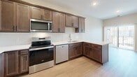 This single-floor unit in Monticello, Minnesota offers a smartly designed layout that maximizes every square foot. Light-toned luxury vinyl plank flooring runs throughout, creating a cohesive and easy-to-maintain foundation across all rooms. The kitchen is a standout feature, outfitted with rich dark-stained cabinetry, white quartz countertops, a classic subway tile backsplash, and a full suite of stainless steel appliances including a range, microwave, refrigerator, and dishwasher. A peninsula counter extends into the living area, providing additional workspace and a natural transition between the kitchen and living room. The living room is bright and open, with a sliding glass door that invites natural light and provides access to an outdoor space. Neutral beige walls and recessed lighting lend a clean, modern ambiance throughout. The bathroom continues the refined aesthetic with a dark-stained vanity, white quartz countertop, brushed nickel fixtures, and a large mirror with overhead lighting. A dedicated laundry room includes a full-size top-load washer and dryer with built-in wire shelving above for added storage. The unit's efficient, open floor plan makes it a practical and comfortable space located in the Monticello community.