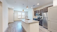 This thoughtfully designed one-bedroom, one-bathroom unit at 651 E Finley Blvd in Anna, TX offers a modern, efficient layout across a single floor. The open-concept kitchen and living area serves as the heart of the unit, highlighted by a large granite-topped island with an undermount sink and stylish gold pendant lighting. The kitchen is fully equipped with dark espresso cabinetry, stainless steel appliances including a refrigerator, range, and microwave, and ample counter space for everyday use. Wood-style plank flooring flows throughout the main living areas, lending a clean and contemporary feel. The living area benefits from multiple windows that allow natural light to fill the space, with a glass-panel entry door providing additional brightness. The bedroom features plush carpet flooring, a ceiling fan, and two windows with outdoor views, creating a comfortable and restful retreat. A dedicated closet offers convenient storage. The full bathroom includes a granite-topped vanity with dark cabinetry, a tub-shower combination with tile surround, and consistent finishes that match the rest of the unit. Additional rooms include a hallway and a utility room, completing this efficiently organized and well-finished living space.