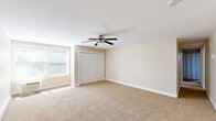 This single-floor home features four bedrooms, one full bathroom, a kitchen, and two hallways, all arranged within a compact and efficient floor plan. The spacious primary bedroom stands out with its generous proportions, soft carpeted flooring, a ceiling fan with light fixture, a double sliding-door closet, and a large window that fills the room with natural light. The remaining three bedrooms are similarly finished with neutral beige carpet, baseboard heating, and closets, offering comfortable and functional spaces. Several bedrooms also feature ceiling fans, adding to the ease of climate control throughout. The kitchen is well-equipped with warm wood cabinetry, a full suite of white appliances including a range, dishwasher, and refrigerator, along with durable dark hardwood-style flooring and ample counter space. The shared bathroom is cleanly finished, highlighted by a tiled tub-and-shower combination featuring a decorative mosaic border accent, chrome fixtures, and crisp white surfaces. Throughout the home, neutral warm-toned walls, white trim, and plush carpeting create a consistent and inviting aesthetic. Baseboard heating is present in multiple rooms, ensuring comfort year-round.